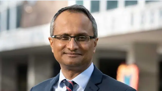 Dr Hashim Ahmed wears glasses and a suit smiling