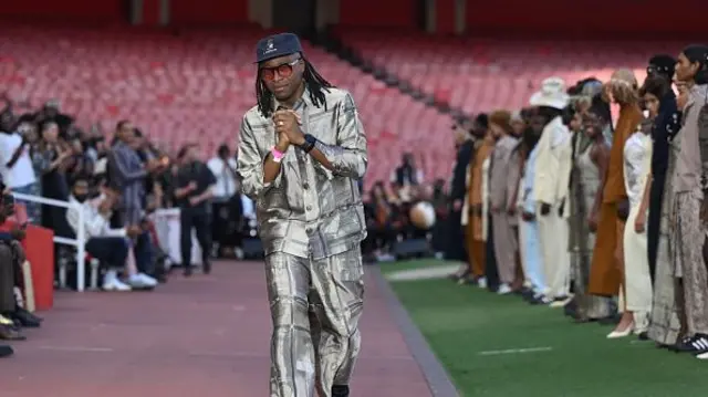 A man in a metallic suit walks up a runway at the Emirates stadium