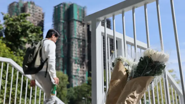 A flower rests against a railing in the foreground with the smouldering high-rise buildings in the background