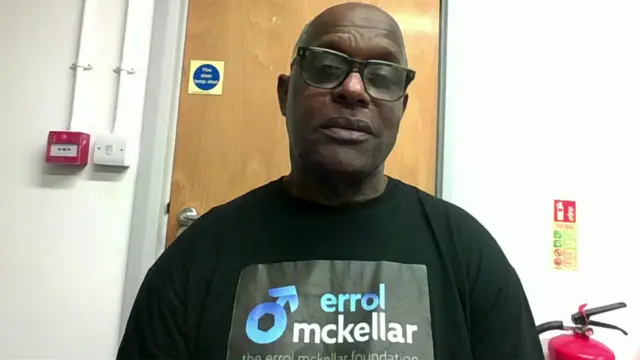 Errol McKellar wears glasses and a t-shirt which bears the name of his charity, 'The Errol McKellar Foundation'