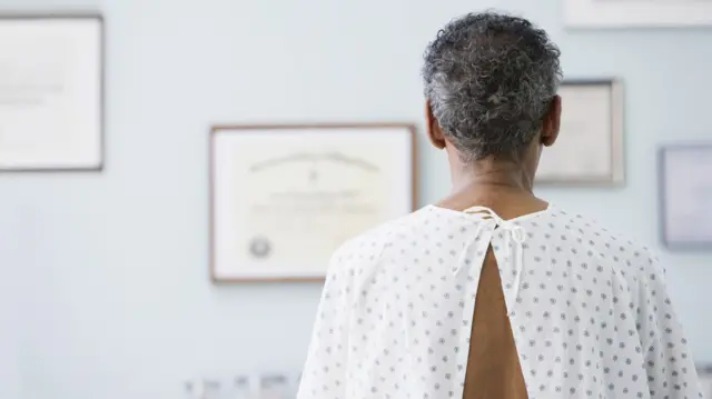 A man wearing hospital gown is sat facing away from the camera