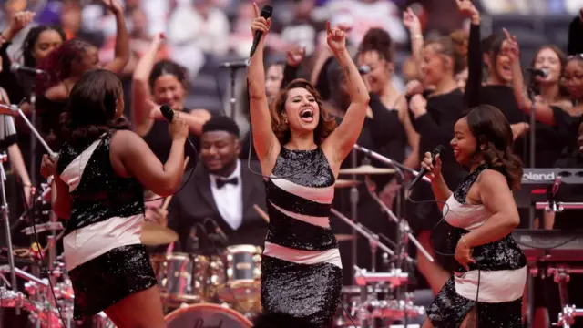 RAYE performing on stage with two backing singers and a drummer