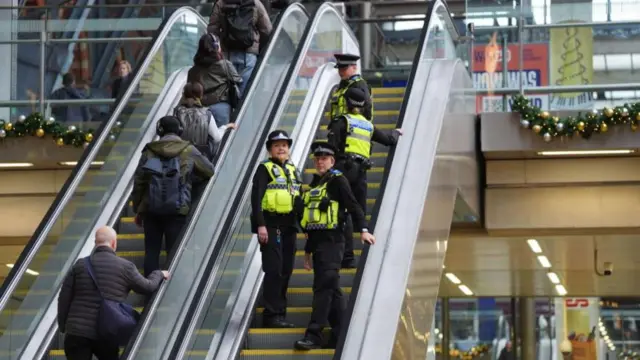 A group of four police officers stand on an escalator