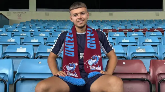 Jonathan Gjoshe sitting in tand, wearing Scunthorpe scarf