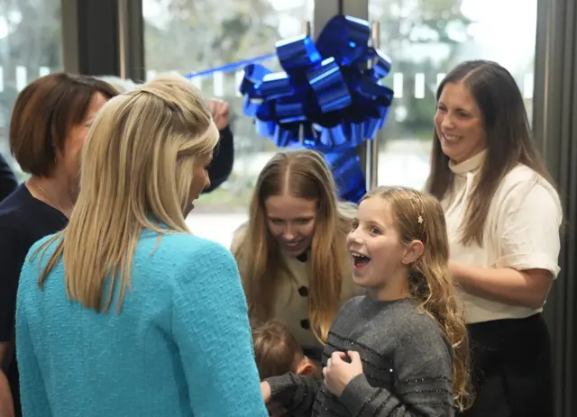 Lindsey Burrow and her children in front of a door with a blue bow on it at the Rob Burrow MND Centre in Leeds