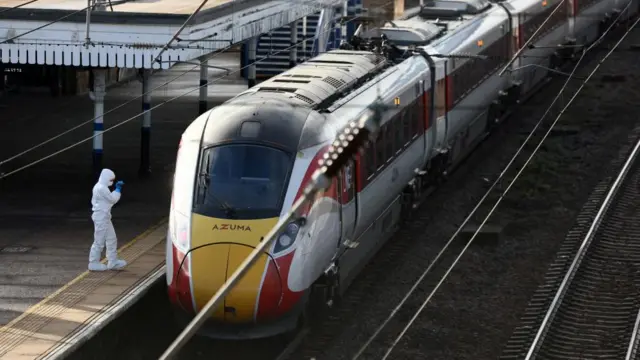 A person in a white forensic suit stands next to a train at a station after a stabbing incident.