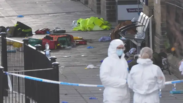 Two people in white suits stand near police tape
