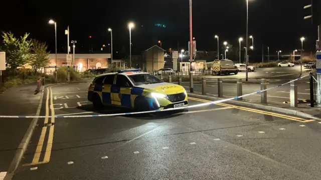 A police car parked next to a police cordon outside the station