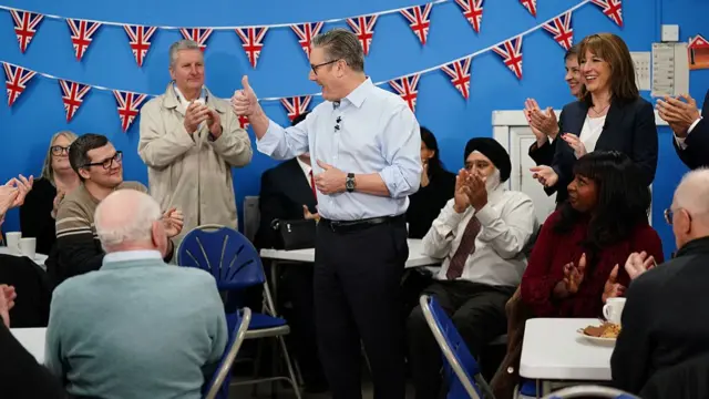 Keir Starmer gives a thumbs up and Rachel Reeves claps as the pair stand in a community centre with other people sitting around clapping