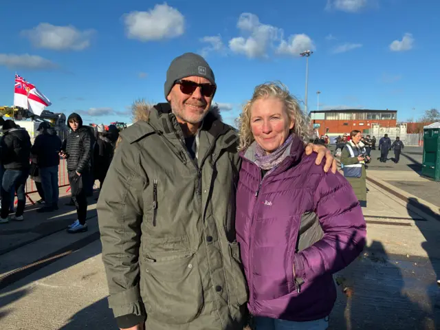 Vicky and Alan Mackinnon stand with their arms around each other looking at the camera and smiling.