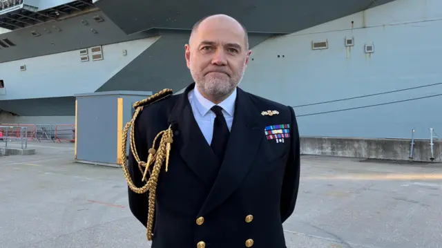Vice Adm Stephen Moorhouse, CBE, stands on Portsmouth naval base in front of HMS Prince of Wales