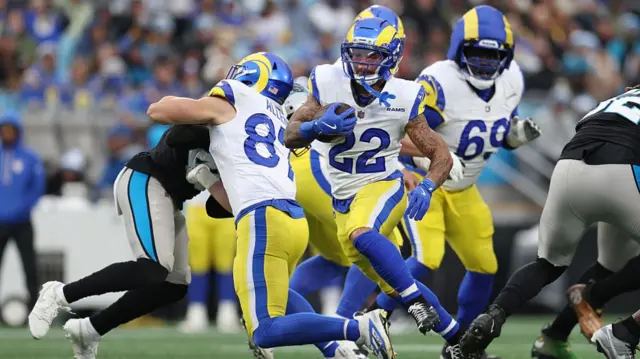 Blake Corum runs with the ball while his team-mates block Panthers defenders all around him.