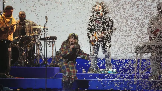 Lola Young performing on stage. Her band are behind her and there is confetti pouring down.