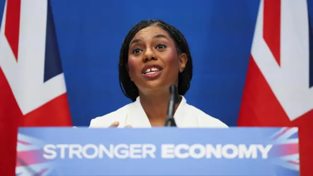 Conservative Party leader Kemi Badenoch giving a speech behind a lectern saying "Stronger Economy" flanked by two union jacks