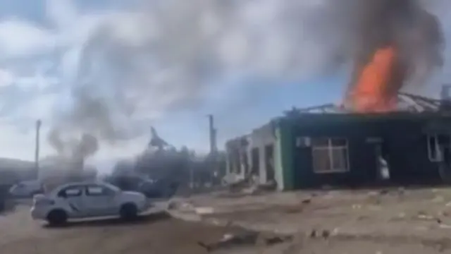 A screengrab from one of the videos showing a building on fire with a distinctive Soviet-era fighter jet mounted on a plinth in the background