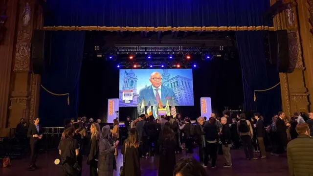 People standing in a large hall with a stage