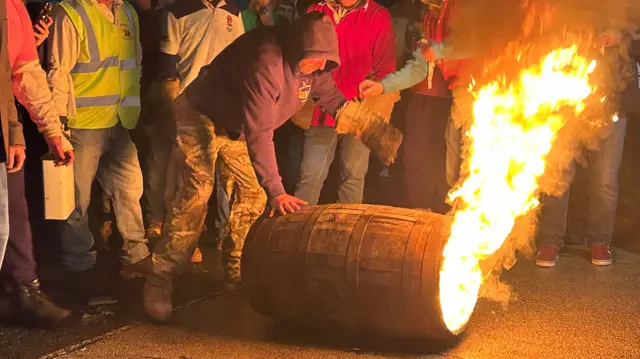 A person rolling a tar barrel on fire.