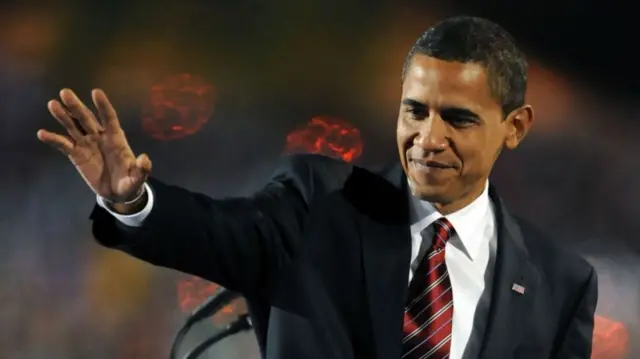 Obama waves at his supporters during his election night victory rally. He wears a suit and striped red tie