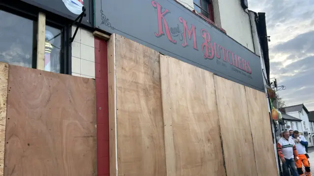 A butcher shop with a boarded up window on the front.