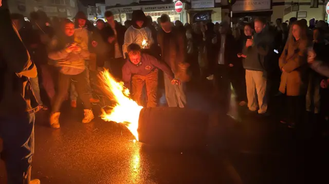 A crowd of people standing around a flaming barrel.