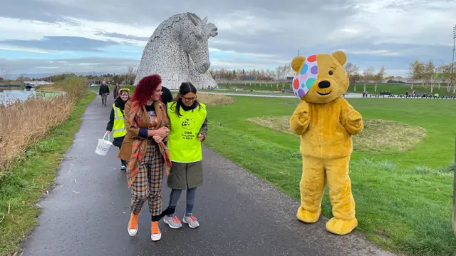 Three-legged walkers in front of giant sculpture of a horse with Pudsey bear