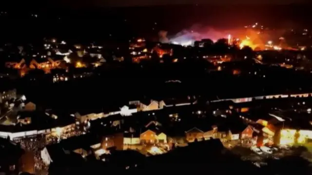 A drone image of crowds and there is a flaming barrel in the middle of it.