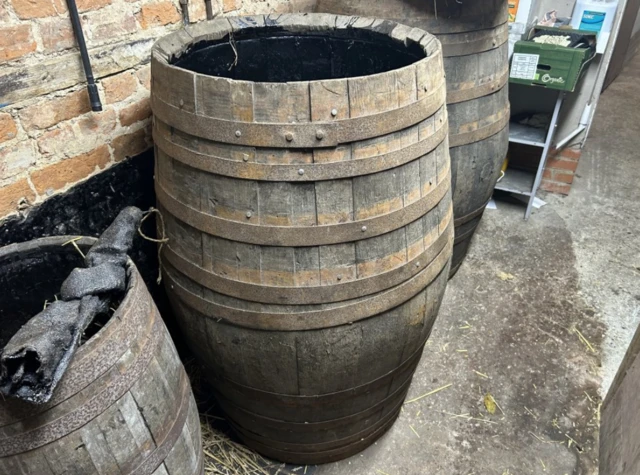 A large barrel stood up-right. There is a smaller one on its left and a larger one on the right. They are wooden and brown.