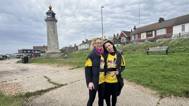 Emily Jeffery and Allison Fern at Shoreham Lighthouse. They are both wearing dark clothes and bright yellow Children in Need T-shirts
