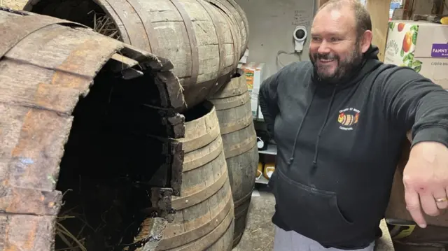 Mike Down stood looking one of the many barrels. He is smiling and wearing a Ottery St Mary Tar Barrel t-shirt.