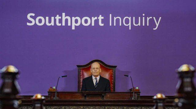 Chairman of the inquiry sitting against a purple backdrop
