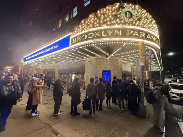 People line up under a brightly lit theatre sign