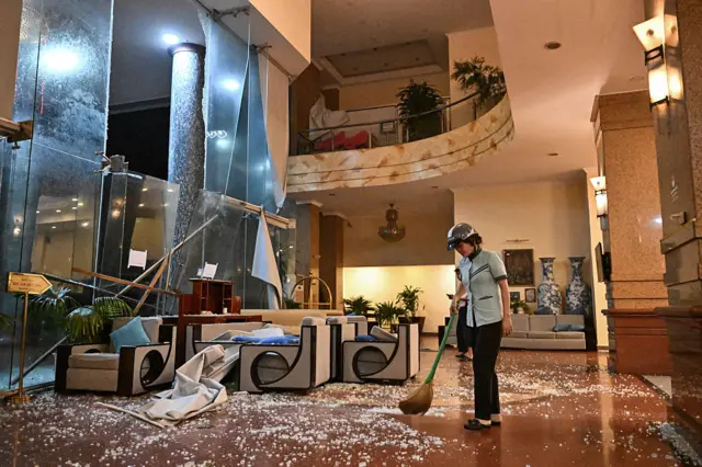 A worker, wearing a helmet, cleans broken glass at a hotel in Vietnam