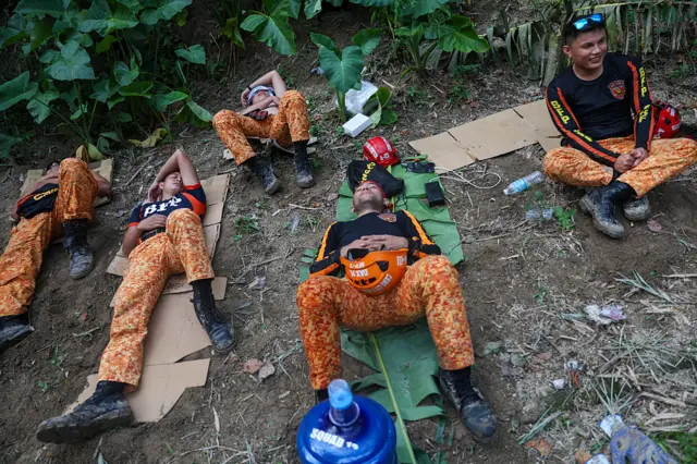 Fatigued rescuers take a break after searching for people inside the rubble of a house damaged in a landslide due to heavy rains caused by Typhoon Kalmaegi in the Philippines