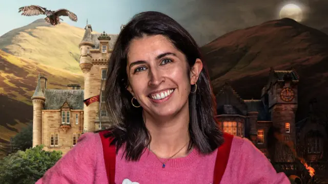 Charlotte is wearing a pink jumper and red dungarees and smiling at the camera. The traitors castle is behind her