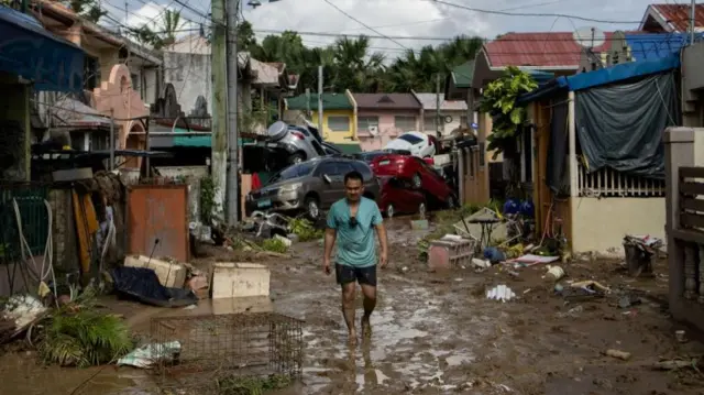 A man walks along a muddy street where cars piled up after being swept away in floods brought by Typhoon Kalmaegi pile up at a subdivision in Bacayan, Cebu Cit