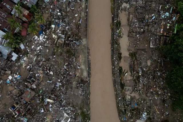 Aerial view of the damage caused by Typhoon Kalmaegi in Talisay, Cebu, Philippines. In the centre of the photo is a river and damaged homes on both sides of it.