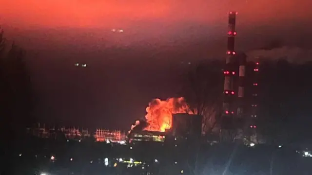 A large fireball visible at a power plant with red and white chimneys next to it