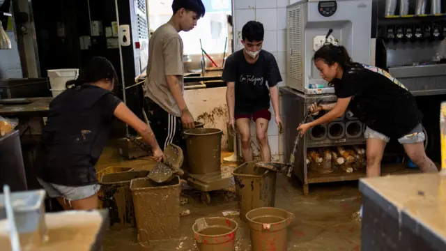 Four workers dress in black t-shirts and shorts remove mud from the floor of McDonald's kitchen with buckets and dustpans.