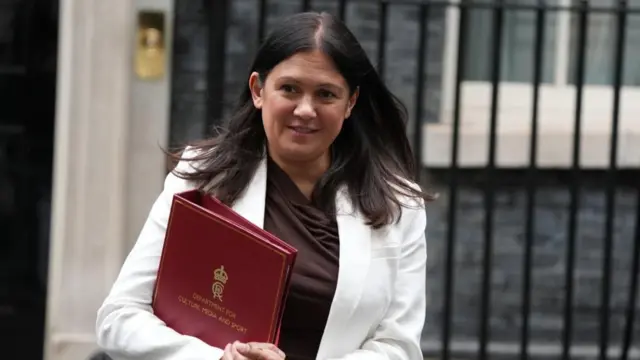 Lisa Nandy, in a white jacket, leaving Downing Street carrying a red folder with Department for Culture, Media and Sport written on it in gold.