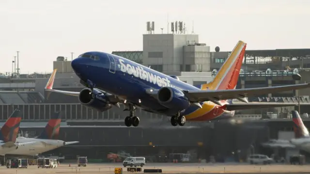 A blue, yellow and red plane takes off from outside a grey airport building