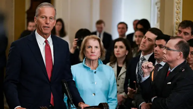 Senate Majority Leader John Thune (R-SD) speaks at a press conference wearing a black suit and red tie