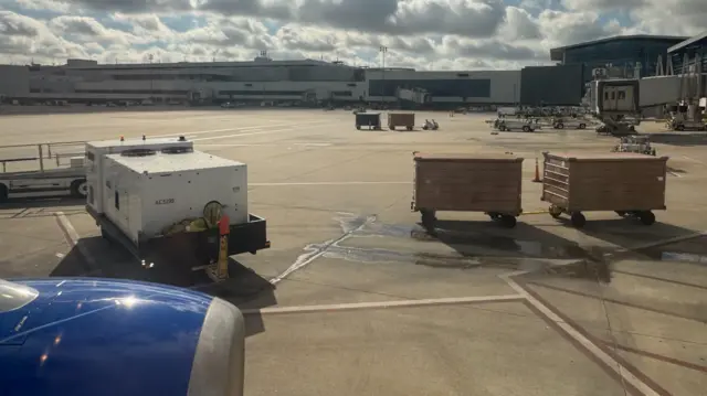 A view of airline baggage carts and an airplane engine from inside the cabin of a United Airlines plane