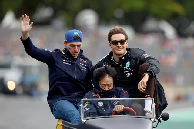 Max Verstappen and George Russell sit on the side of a mini car while Yuki Tsunoda drives