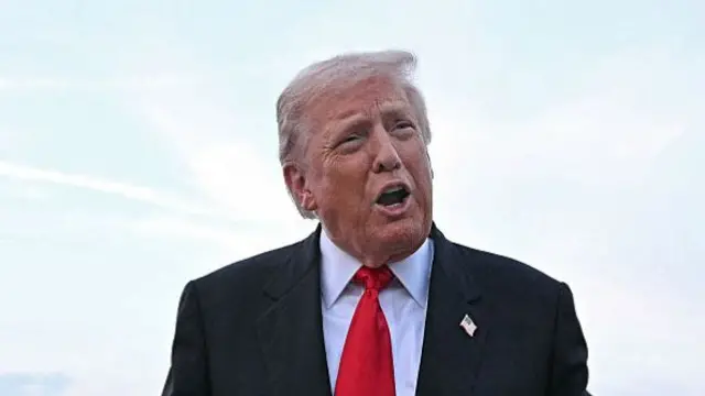 Trump is outdoors. background is sky which looks white. He is wearing a red tie.
