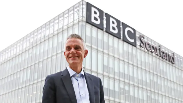Tim Davie standing in front of a building with the BBC logo