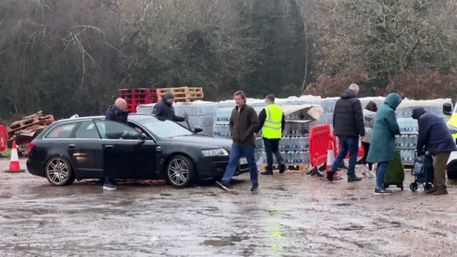 People at a car park with piles of water bottles in the rain