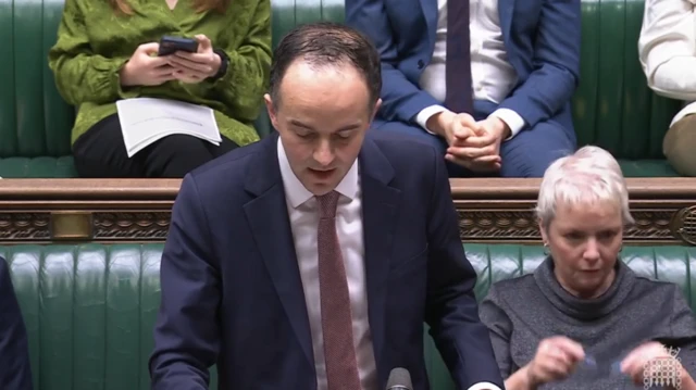 James Murray is wearing a navy suit with a burgundy tie, whilst addressing the House of Commons