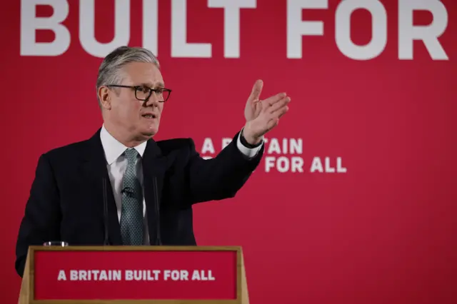 Sir Keir Starmer raises his right arm as he stands behind a red podium that reads: "A Britain for all"