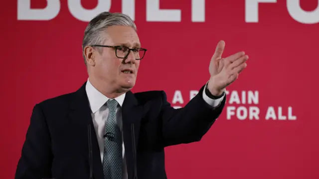 Prime Minister Sir Keir Starmer standing in front of a red background at a podium that reads "a Britain built for all"