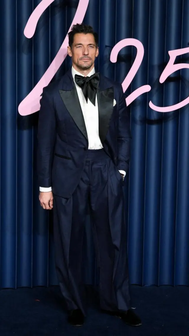 Model David Gandy wears a deep-bue tuxedo with an oversized, black bow-tie
